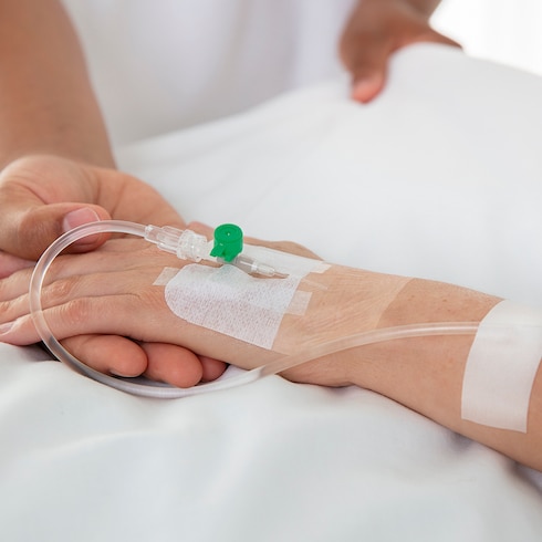 Verpleegkundige die de hand van de patiënt vasthoudt met close-up van Leukomed I.V.-film van Leukoplast